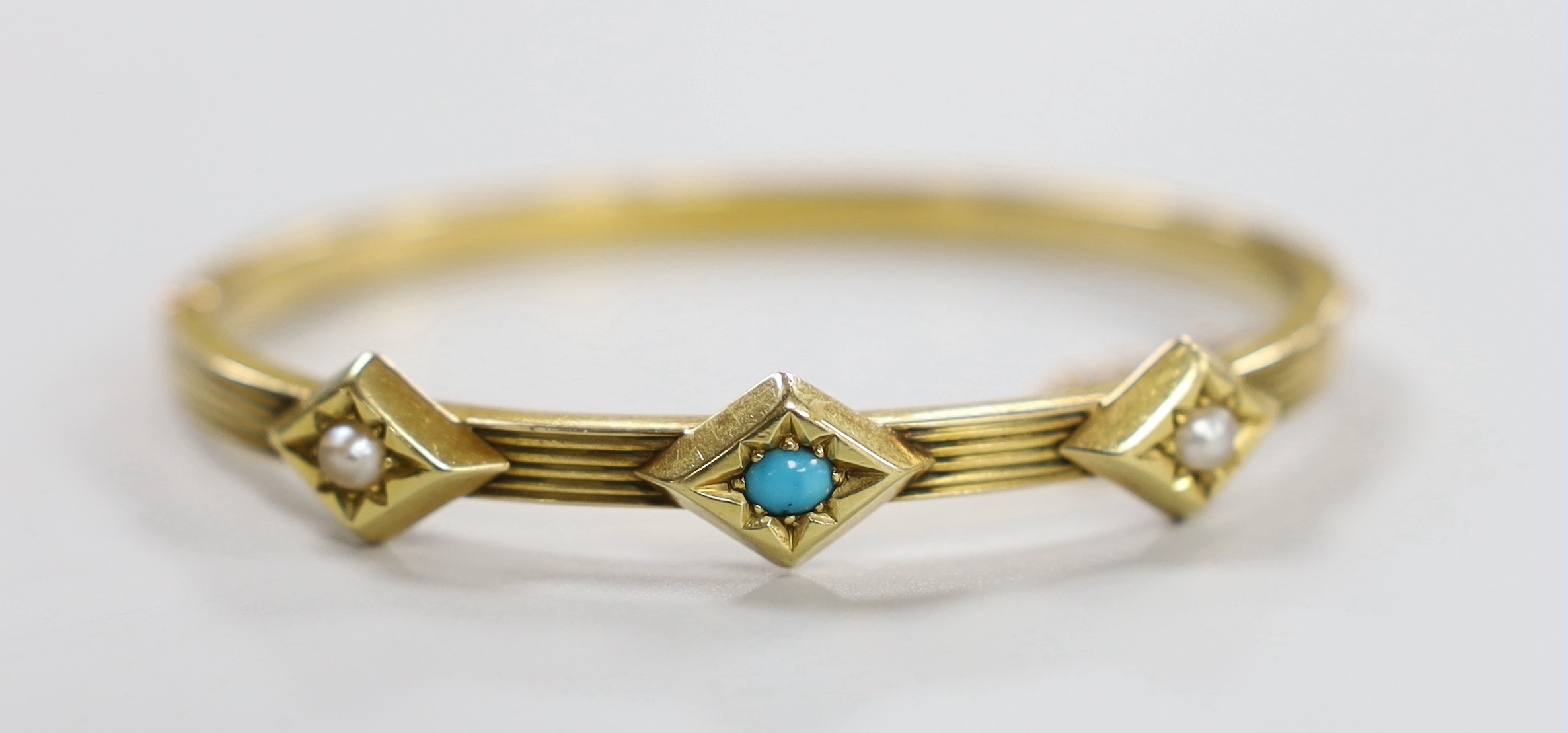 An Edwardian reeded yellow metal, turquoise and split pearl set three stone hinged bangle, interior diameter 56mm, gross weight 11.6 grams.